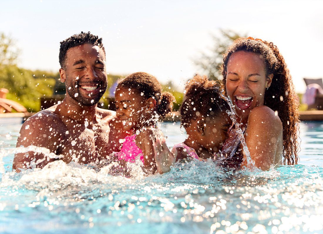 Personal Insurance - Family on Summer Holiday With Two Girls Being Held in a Swimming Pool by Their Parents and Splashing